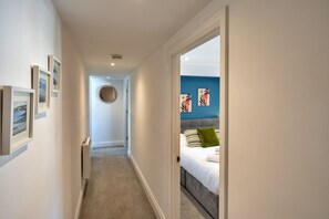 Ein Flur, der in ein Schlafzimmer mit einem Bett, einem Heizkörper und gerahmten Bildern an der Wand führt.