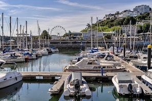 Un port de plaisance avec des bateaux amarrés, une grande roue en arrière-plan et des bâtiments sur une colline.