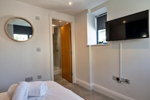 A hotel room with a bed, a TV mounted on the wall, a mirror, and a door leading to a shower area. - Finest Retreats | Harbour View (Torquay)