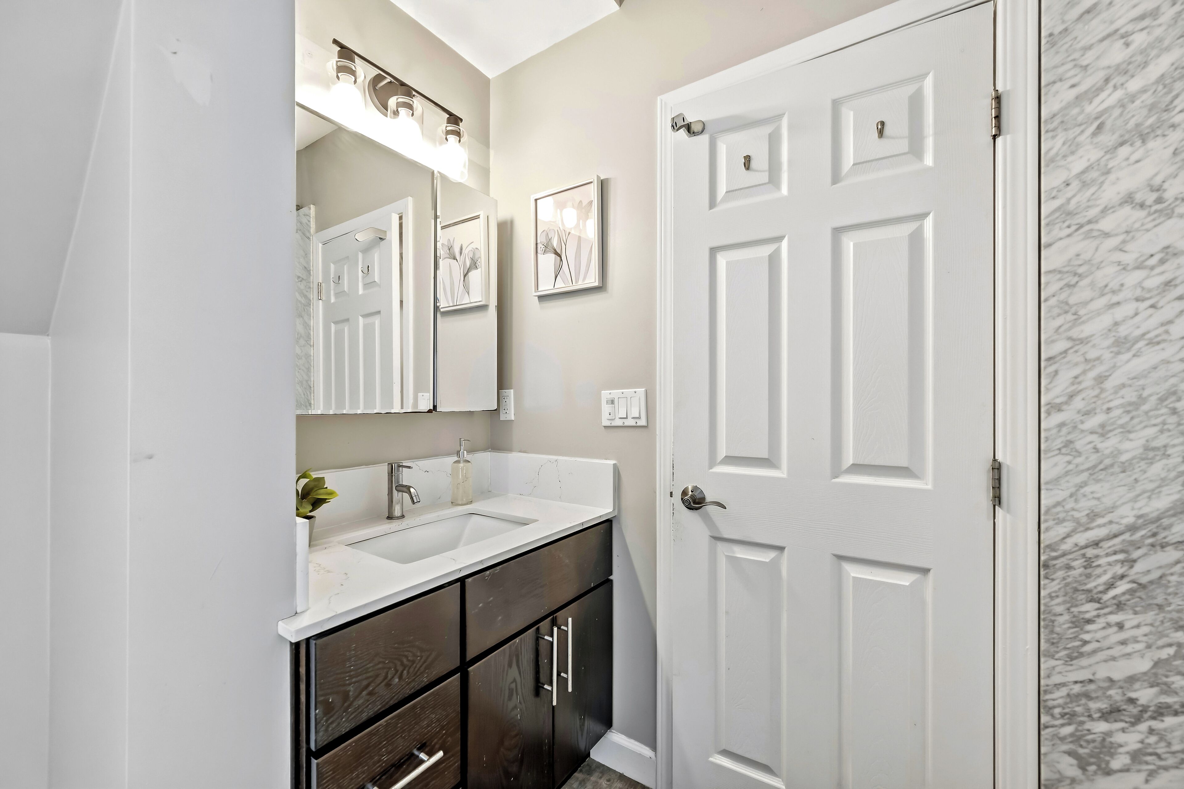 A bathroom with a white door, a double sink vanity, a mirror, and a marble wall.