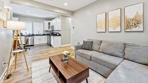 A modern living room with a sofa, coffee table, and a lamp. A kitchen is visible in the background. - Modern 5BR House with AC in Central Berkeley (Berkeley)