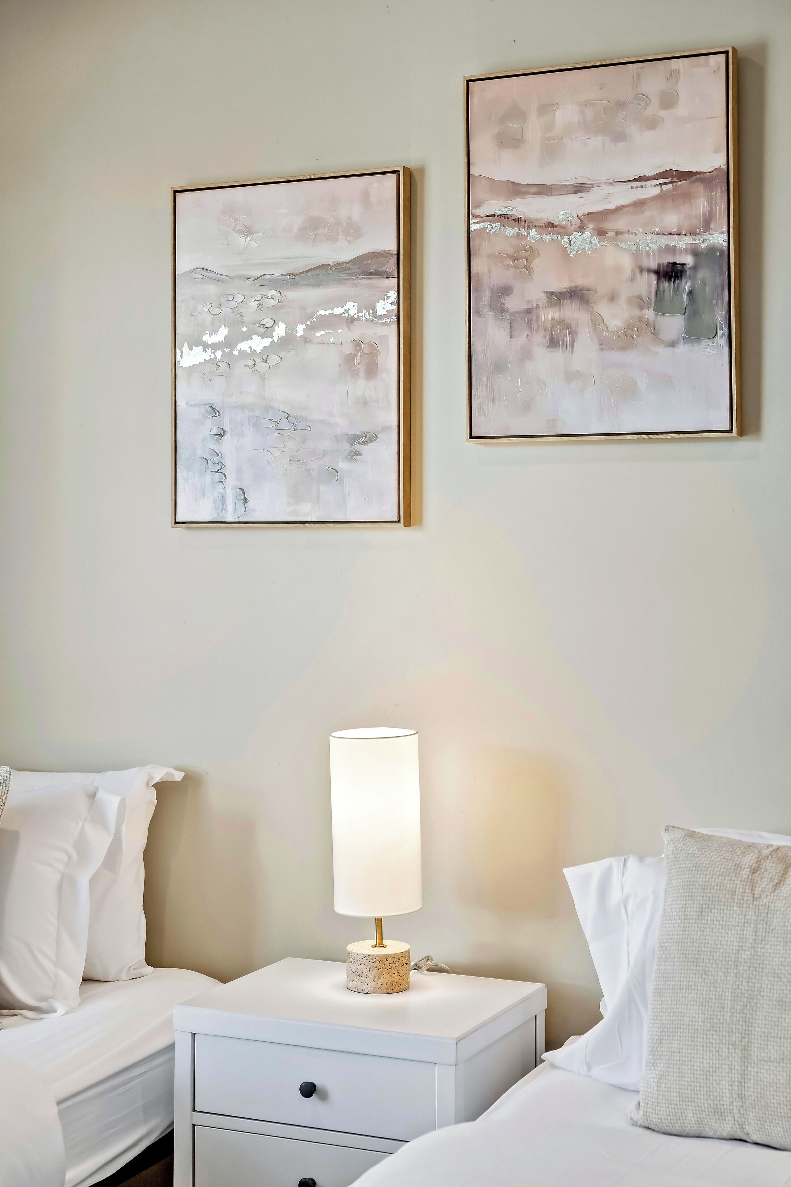 Une chambre d’hôtel avec deux lits, une table de chevet avec une lampe et deux tableaux abstraits accroch és au mur.