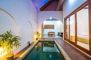 A pool area with a wooden deck, a dining table, and chairs, and a view into a room with a bed. - Andorra Villa Nusa Dua (Badung)