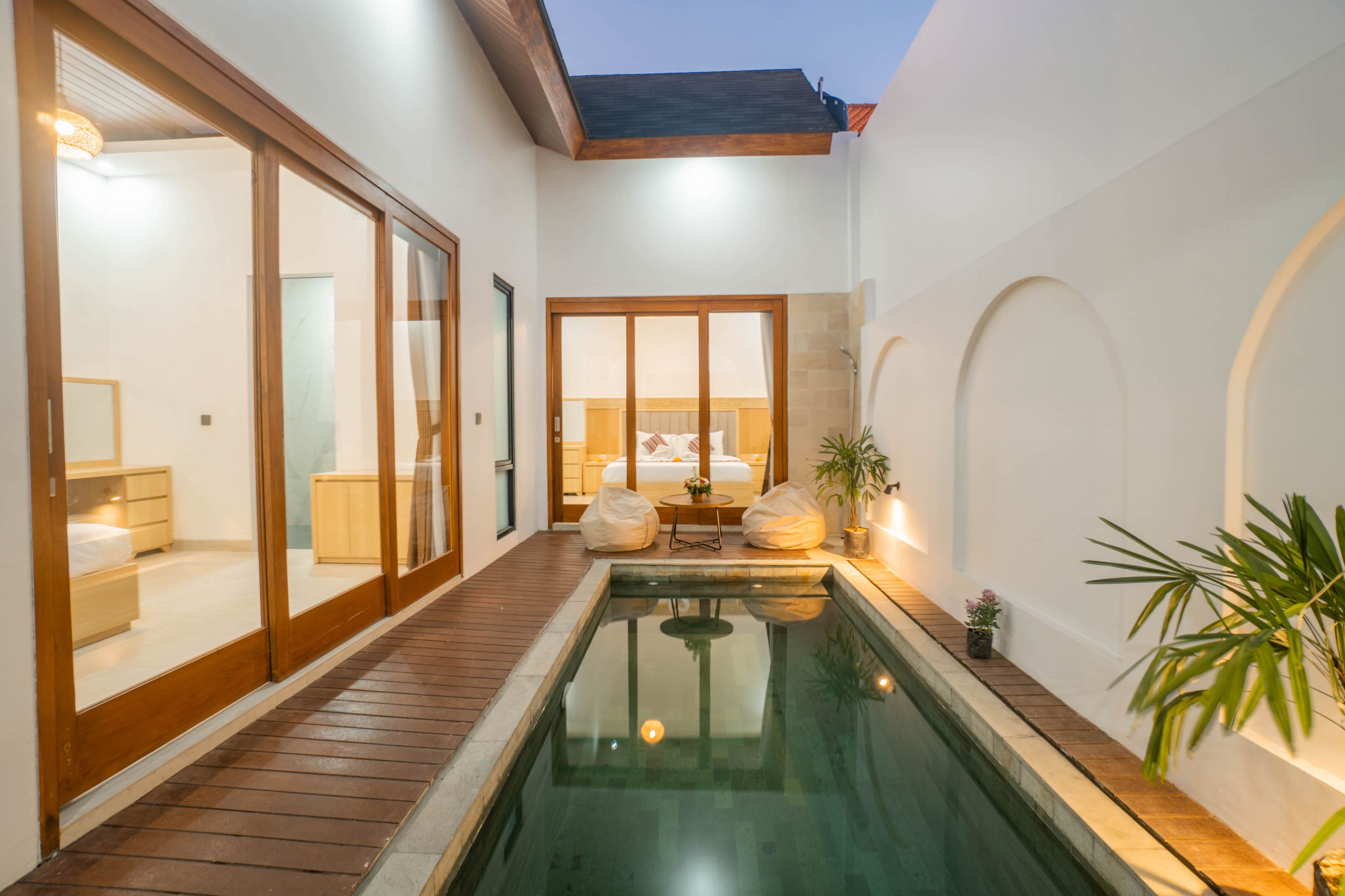 A modern hotel room with a large sliding glass door, a small pool, and a cozy seating area with cushions.