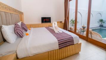 A hotel room with a bed, a television, a view of a swimming pool, and a balcony with plants.