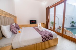 A hotel room with a bed, a television, a view of a swimming pool, and a balcony with plants. - Andorra Villa Nusa Dua (Badung)