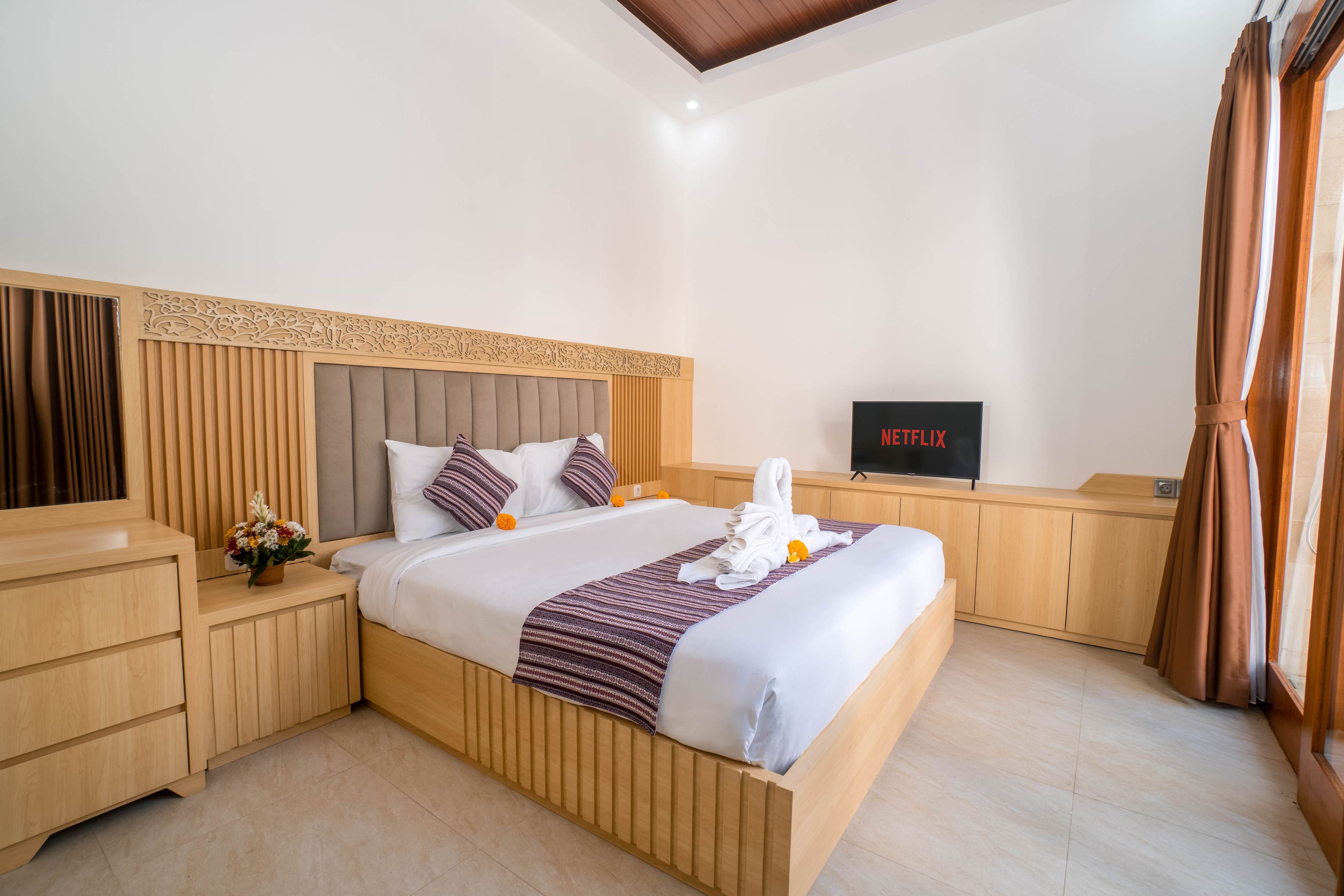 Habitación de hotel con una cama, un televisor, una mesita de noche de madera y una ventana con cortinas.