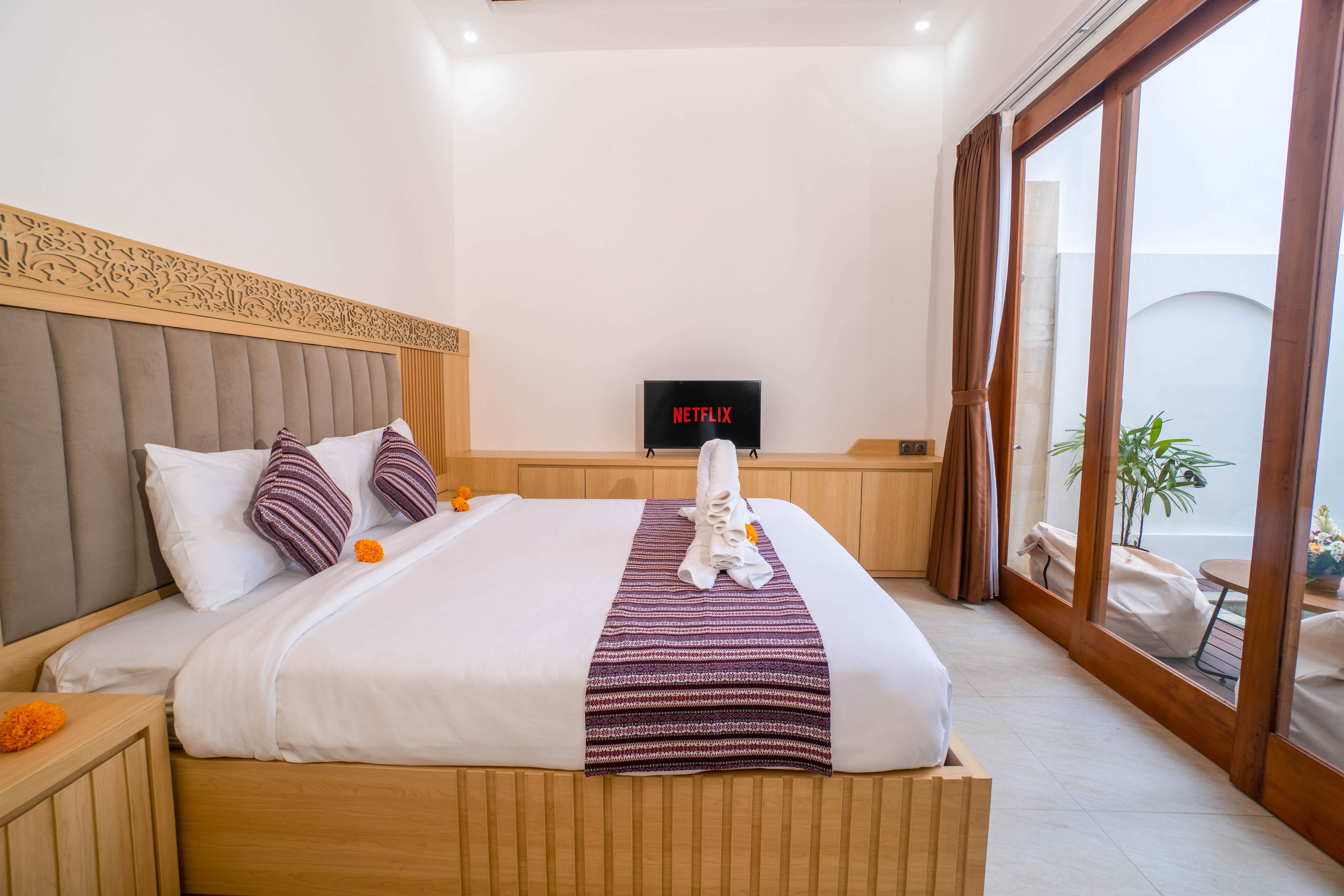A hotel room with a large bed, a flat-screen TV, a wooden headboard, and a view of the outdoors.