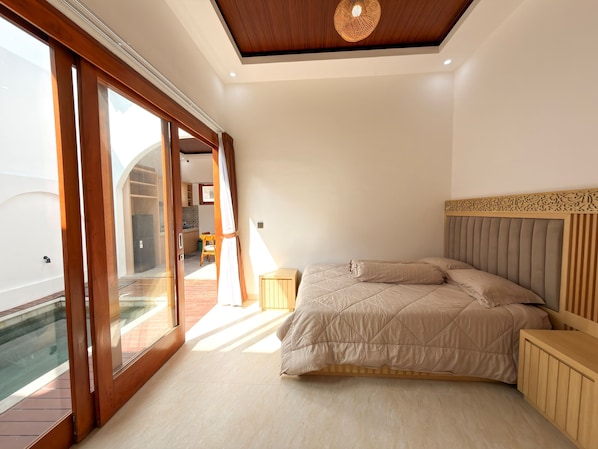 A bedroom with a bed, wooden headboard, and a view of a pool and outdoor area. - Andorra Villa Nusa Dua (Badung)