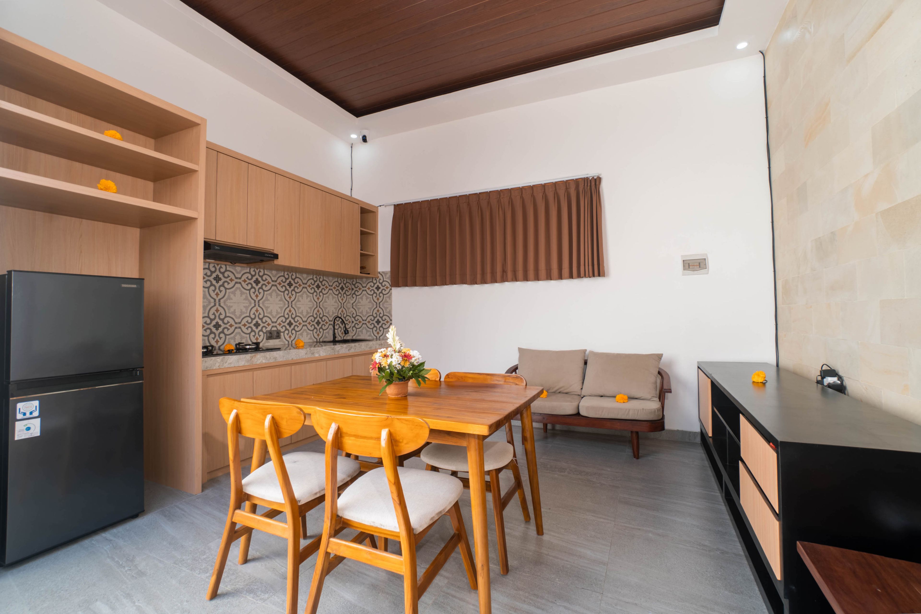 A compact kitchen with a refrigerator, wooden cabinets, and a tiled backsplash.