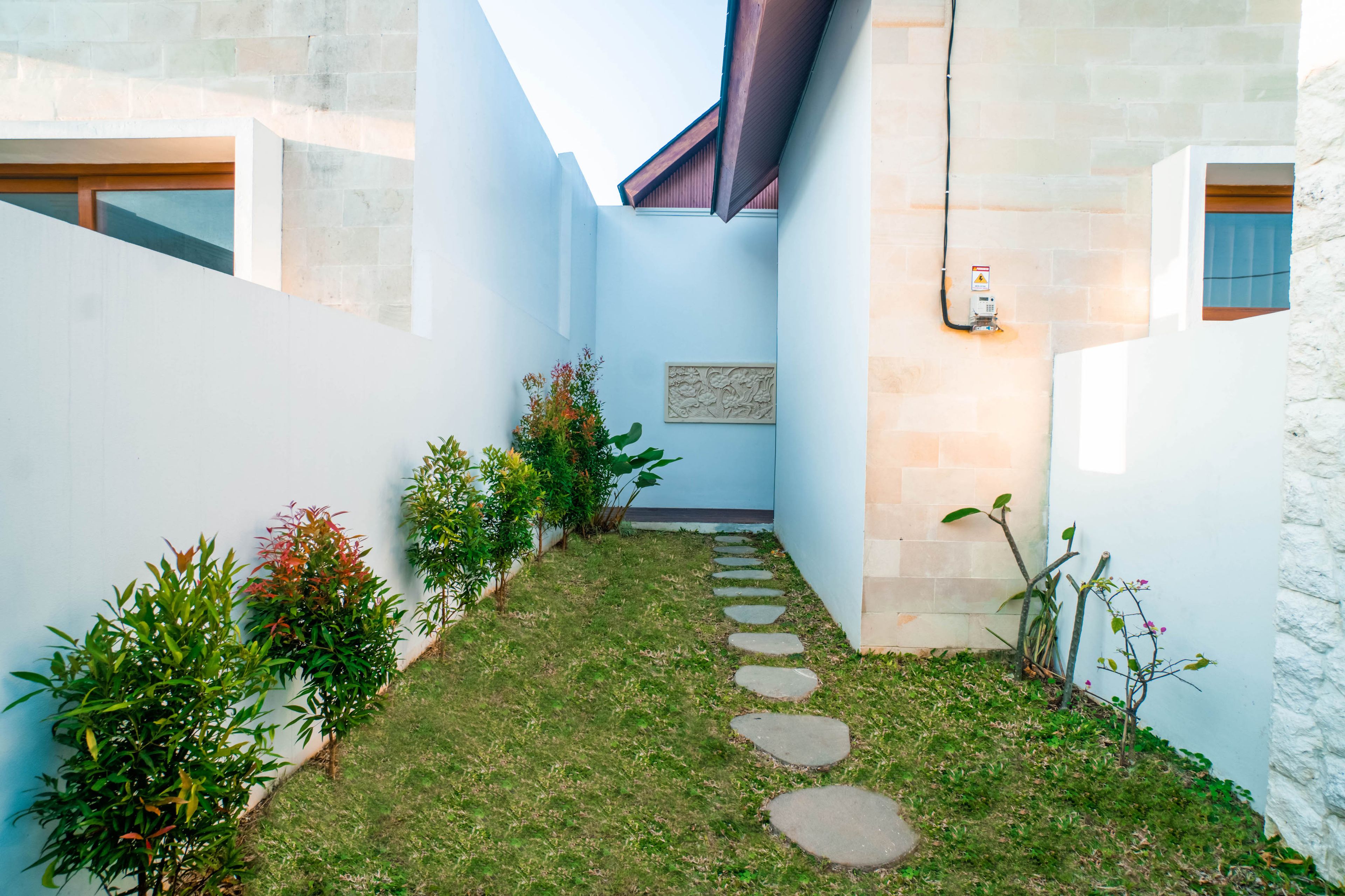 A narrow courtyard with a stone pathway, surrounded by walls and plants.