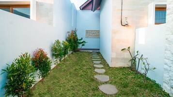 A narrow courtyard with a stone pathway, surrounded by walls and plants.