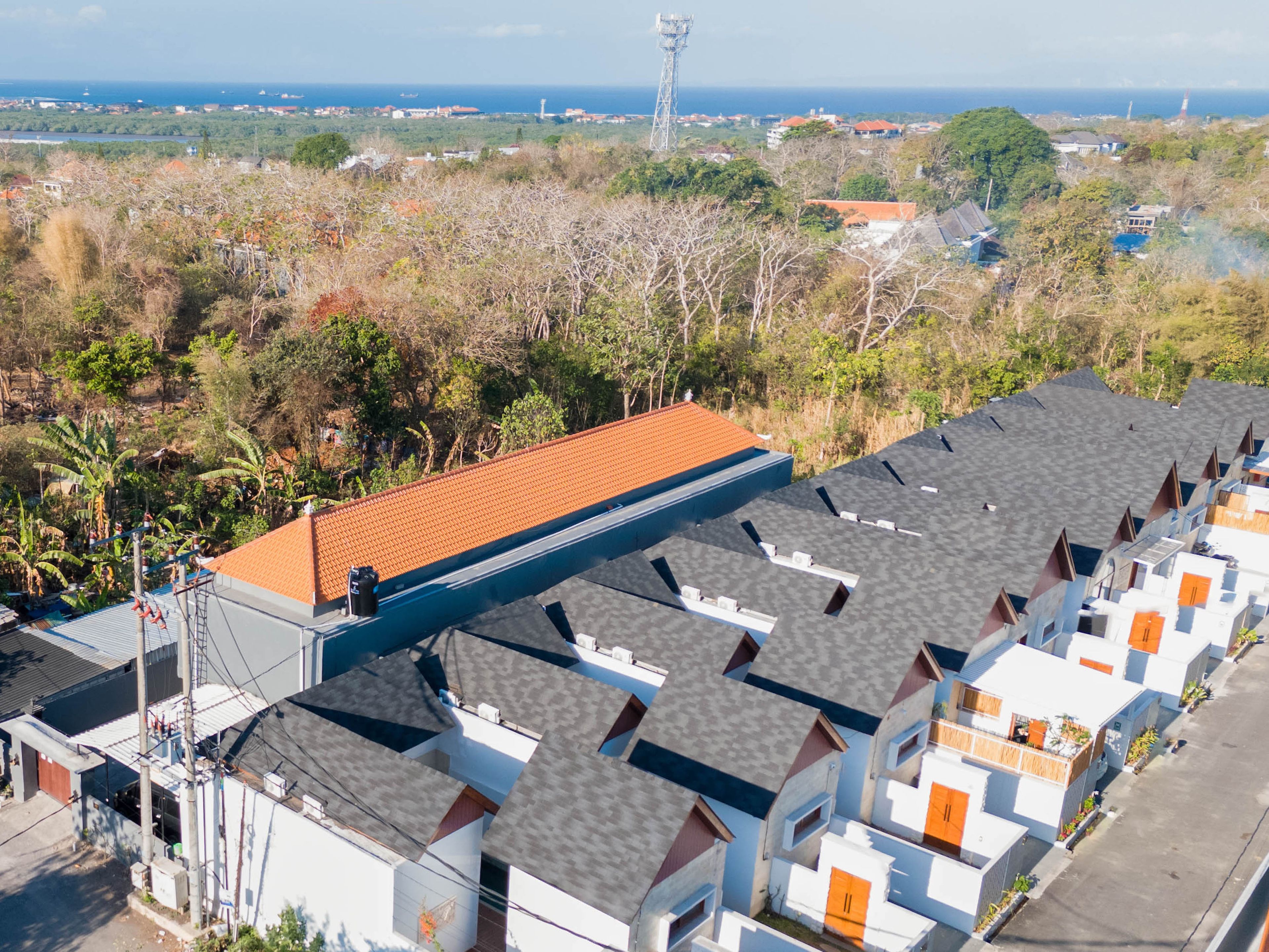 A residential area with multiple houses, a prominent red-roofed building, and a clear view of the ocean.