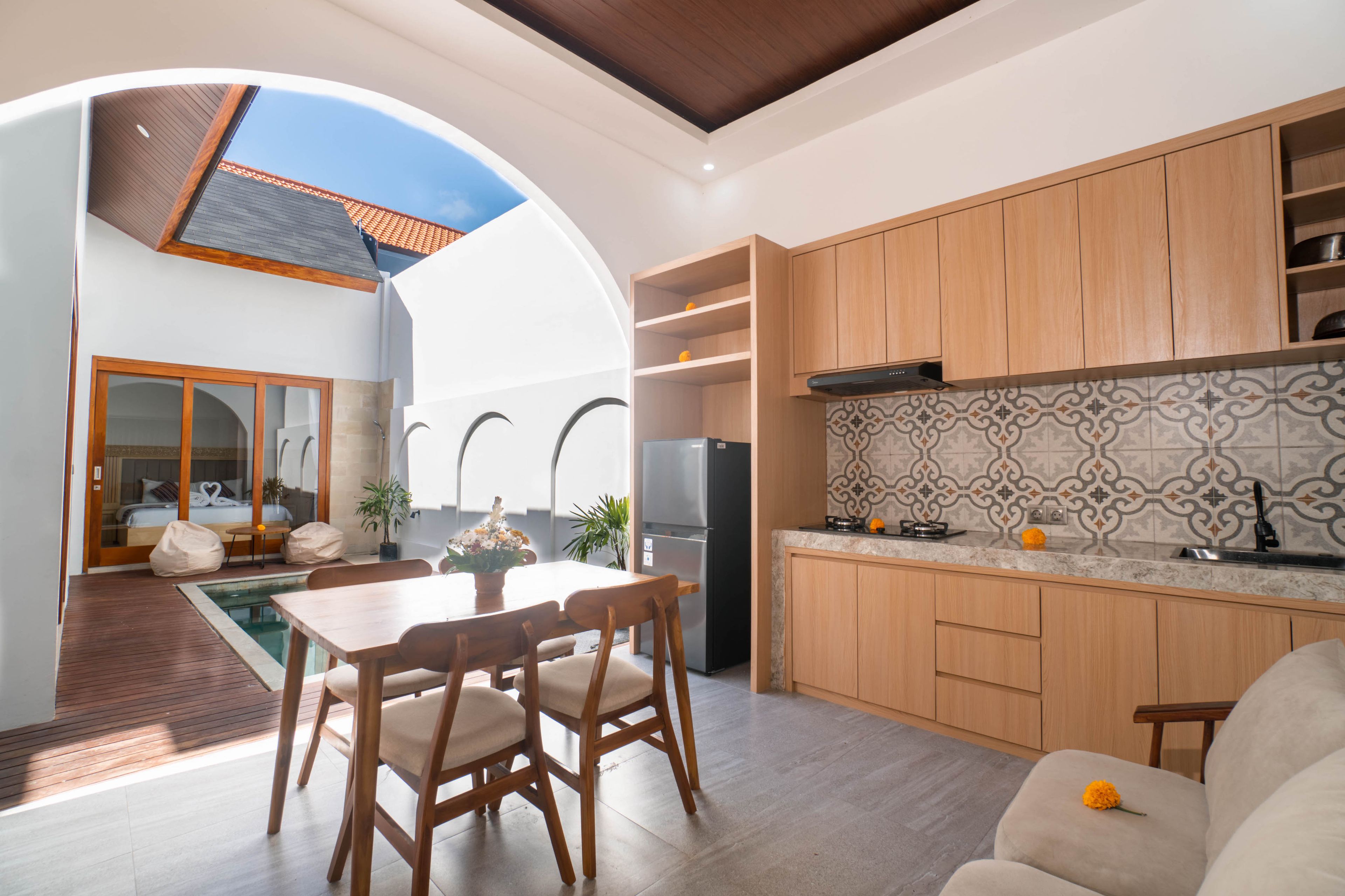 A modern kitchen with wooden cabinets, a tiled backsplash, and a dining area with a pool view.