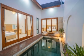A modern hotel room with a glass-enclosed balcony, a pool, and a separate bedroom visible through the glass doors. - Andorra Villa Nusa Dua (Badung)