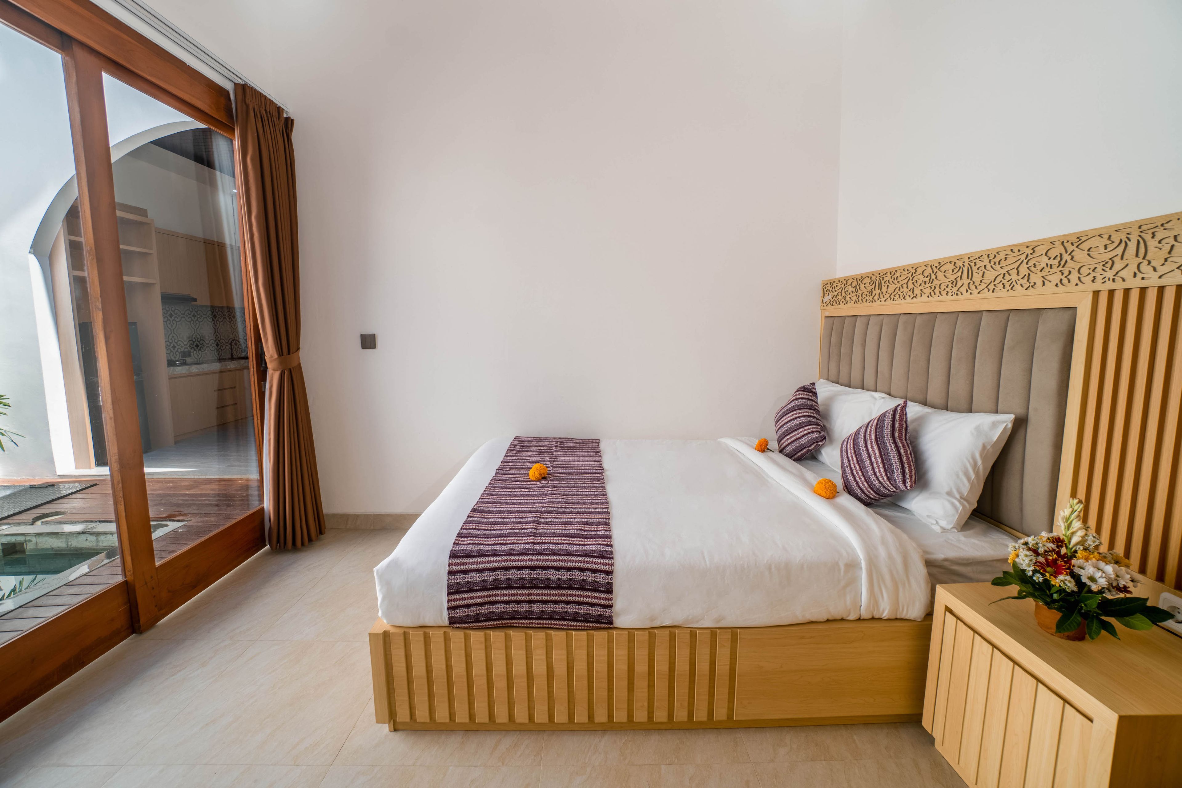 A hotel room with a large bed, wooden headboard, and a view of a pool through a sliding glass door.