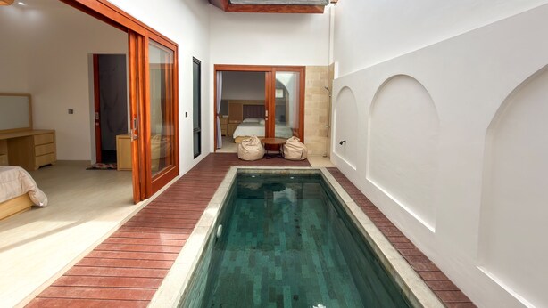 Ein modernes Hotelzimmer mit Pool, Holzboden und einer Schiebeglastür, die auf einen Balkon führt.