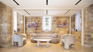 A modern living room with stone walls, a beige sofa, two armchairs, a coffee table, and artwork on the walls. - Unique Luxury 3BR Duplex on HaNeviim-Private Pool and Free Parking (Jerusalem)