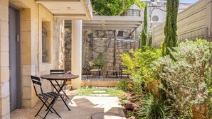 A courtyard with a stone wall, a wooden table and chairs, and a variety of plants. - Unique Luxury 3BR Duplex on HaNeviim-Private Pool and Free Parking (Jerusalem)