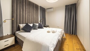 A modern bedroom with a bed, bedside tables, a nightstand, a wall-mounted air conditioner, and a ceiling light fixture. - Unique Luxury 3BR Duplex on HaNeviim-Private Pool and Free Parking (Jerusalem)