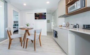 Una cocina moderna con microondas, lavamanos y armarios de madera. Hay una zona de comedor con mesa y sillas.