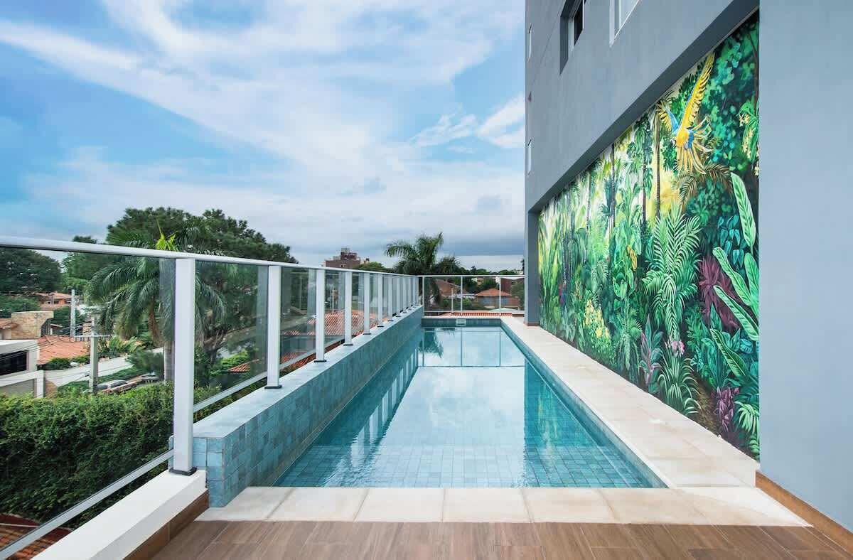 A rooftop swimming pool with a glass railing, surrounded by a tropical mural.