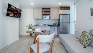 Una cocina moderna equipada con microondas, cafetera y refrigerador. Hay un comedor con mesa y sillas, y un sofá con un cojín estampado.