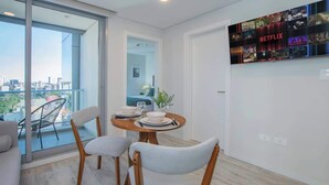 A modern living room with a dining area, a balcony with a city view, and a wall-mounted Netflix display. - Corporate Stays Unico - 1401 - 1Br (Asunción)