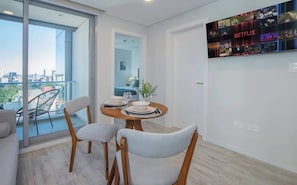 Ein modernes Wohnzimmer mit Essbereich, ein Balkon mit Blick auf die Stadt und einem an der Wand montierten Netflix-Display.