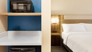 A hotel room with a microwave on a shelf, a bedside table with a lamp, and a bed with white bedding. - Holiday Inn Express Knoxville Airport Alcoa by IHG (Alcoa)