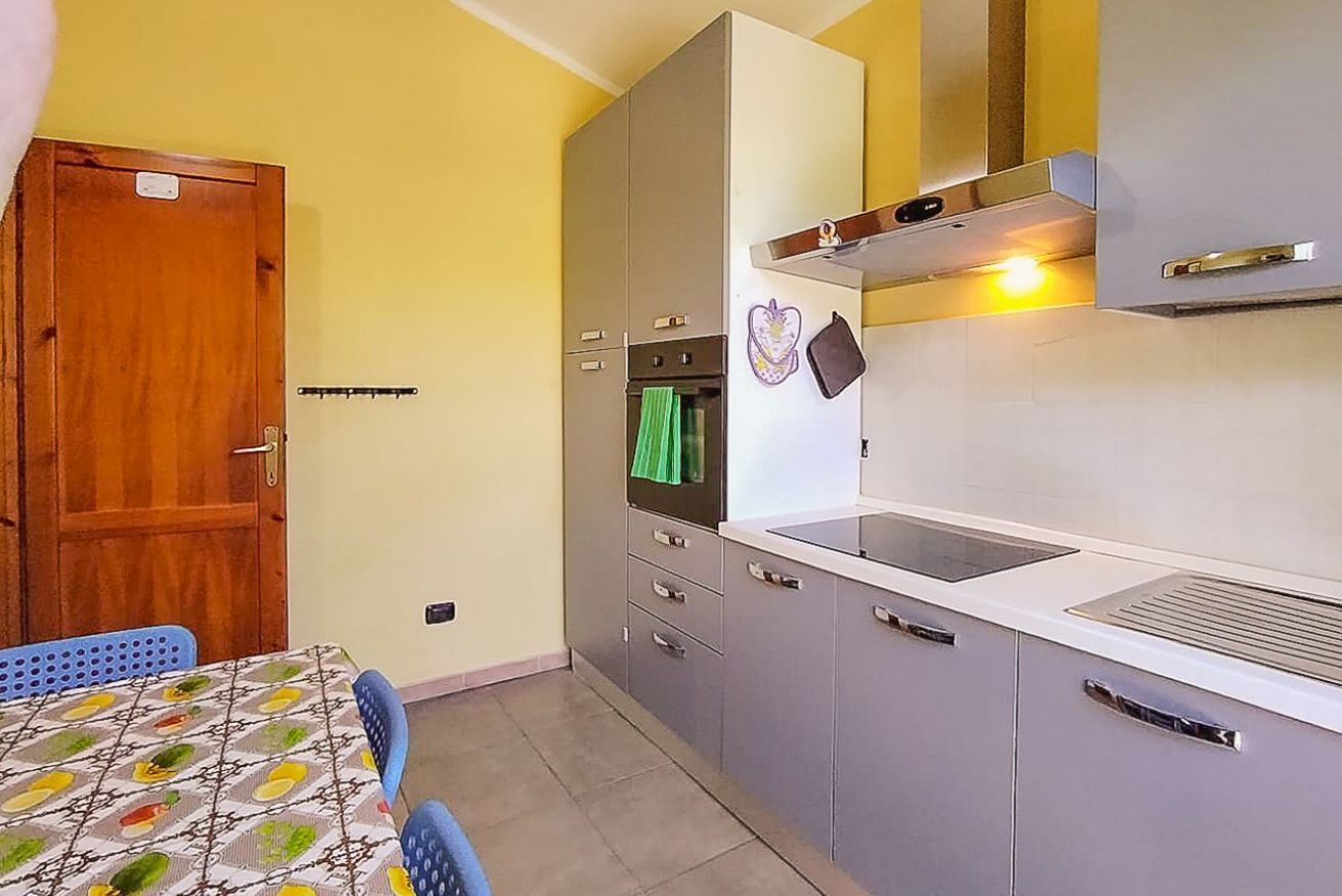 Une cuisine de taille réduite avec une porte en bois, une table à manger recouverte d’une nappe à motifs et un four encastré.