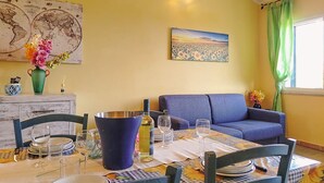 A dining area with a table set for four, a blue sofa, a world map artwork, and a sunset painting. - Between Sea & Nature – 3 Minutes from La Pelosa (Stintino)