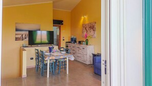 A dining area with a TV, a table with chairs, a cabinet, and a wall with a world map. - Between Sea & Nature – 3 Minutes from La Pelosa (Stintino)