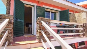 A building with a stone facade, green shutters, and a balcony with a table and chairs. - Between Sea & Nature – 3 Minutes from La Pelosa (Stintino)