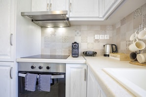 A kitchen with white cabinets, a stainless steel range, a built-in oven, a coffee maker, and a mug rack. - Themis Apartment (Kalamata)