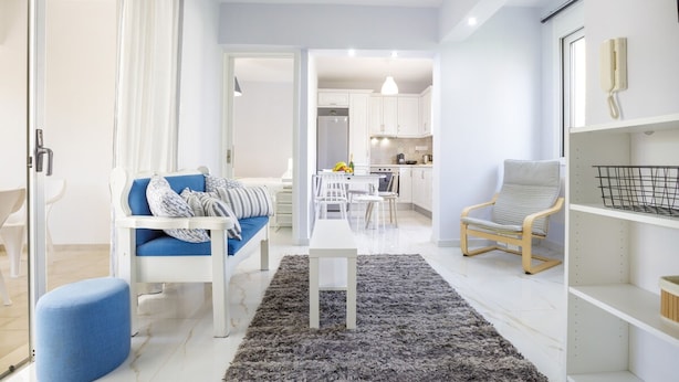 Ein modernes Wohnzimmer mit einer Couch, einem Couchtisch und einem Sessel. Im Hintergrund ist eine Küchenzeile mit Schränken und einem Esstisch zu sehen.