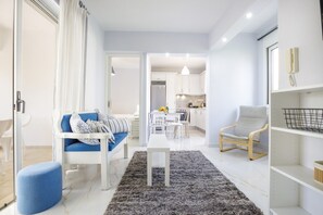 Ein modernes Wohnzimmer mit einer Couch, einem Couchtisch und einem Sessel. Im Hintergrund ist eine Küchenzeile mit Schränken und einem Esstisch zu sehen.