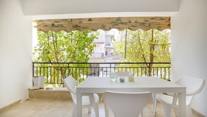 Ein Balkon mit einem weißen Tisch und Stühlen, einem schwarzen Geländer und Blick auf Bäume und Gebäude.