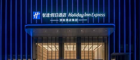 Entrada de un hotel Holiday Inn Express con diseño moderno, destacando una fachada de vidrio y un letrero de neón azul.