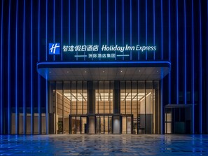 A Holiday Inn Express hotel entrance with a modern design, featuring a glass facade and a blue neon sign.