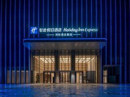 Entrada de un hotel Holiday Inn Express con diseño moderno, destacando una fachada de vidrio y un letrero de neón azul.