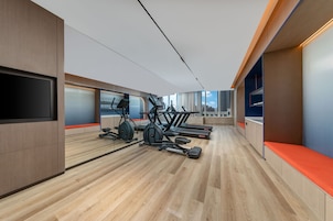 Un gimnasio moderno con equipo de ejercicio, suelo de madera y un amplio ventanal con vistas a la ciudad.