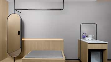 Una habitación moderna y minimalista con cama, un pequeño escritorio, un espejo y un armario empotrado.