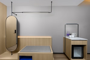 A modern, minimalist room with a bed, a small desk, a mirror, and a built-in cabinet.