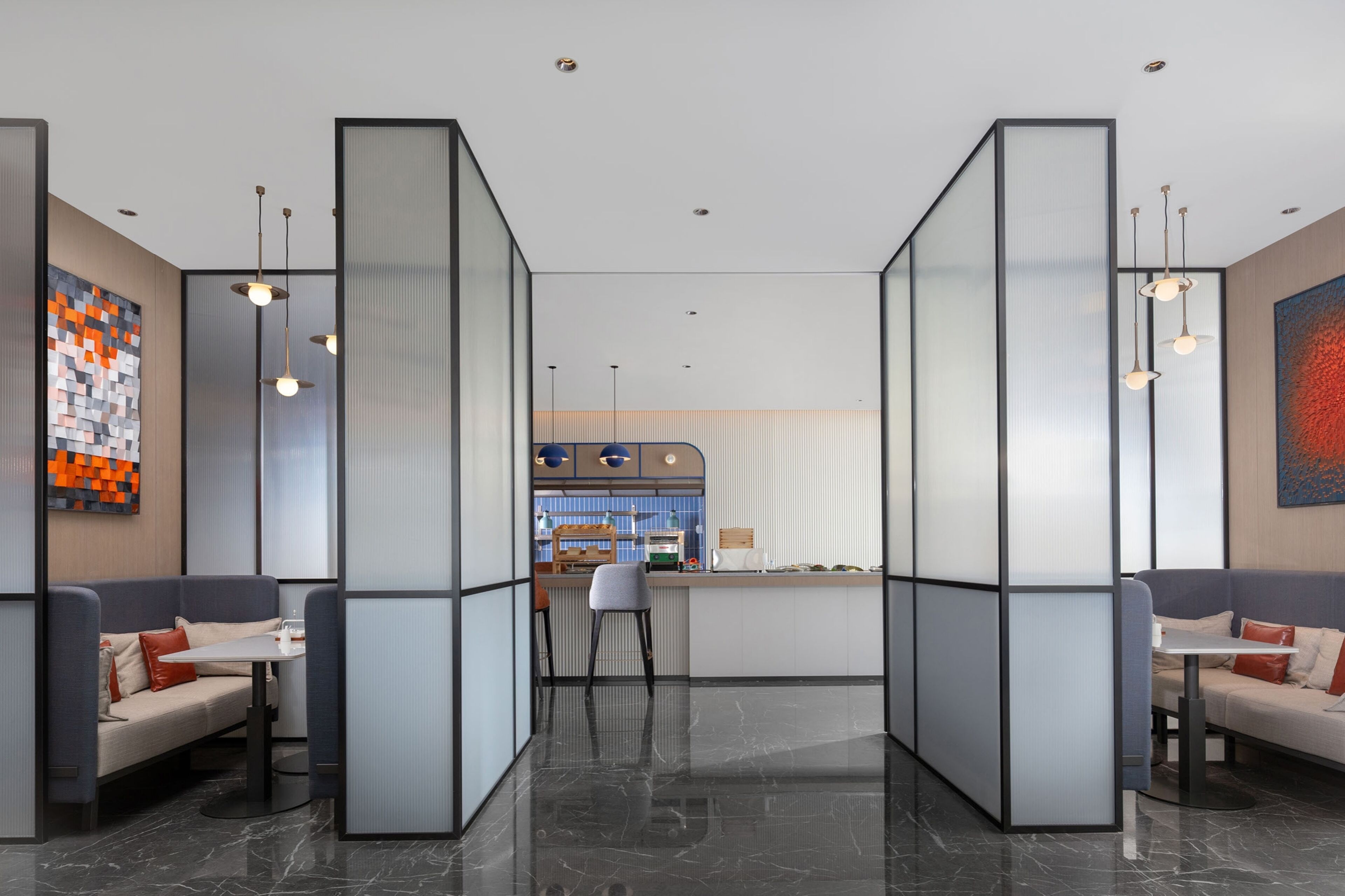 Un hall d’hôtel moderne avec des espaces aménagés pour s’asseoir, un comptoir d’accueil et une cuisine en arrière-plan.