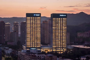 Two high-rise buildings with illuminated windows, surrounded by other buildings and a mountainous backdrop. - Holiday Inn Express Rui An Xincheng by IHG (Wenzhou)