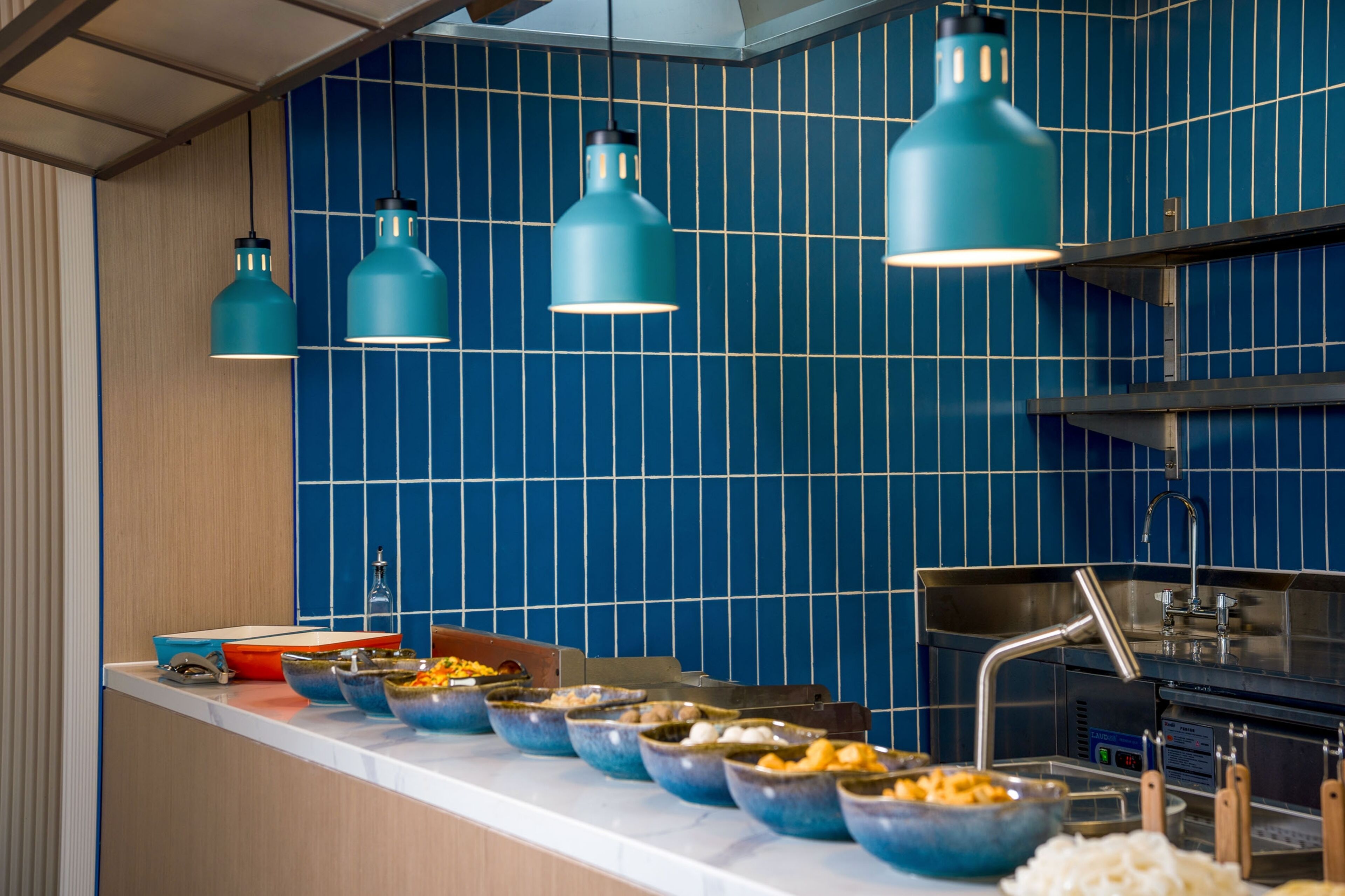 Tarjolla on runsas buffet, jossa on useita erilaisia ruokalajeja, pesuallas ja siniset riippuvalaisimet.