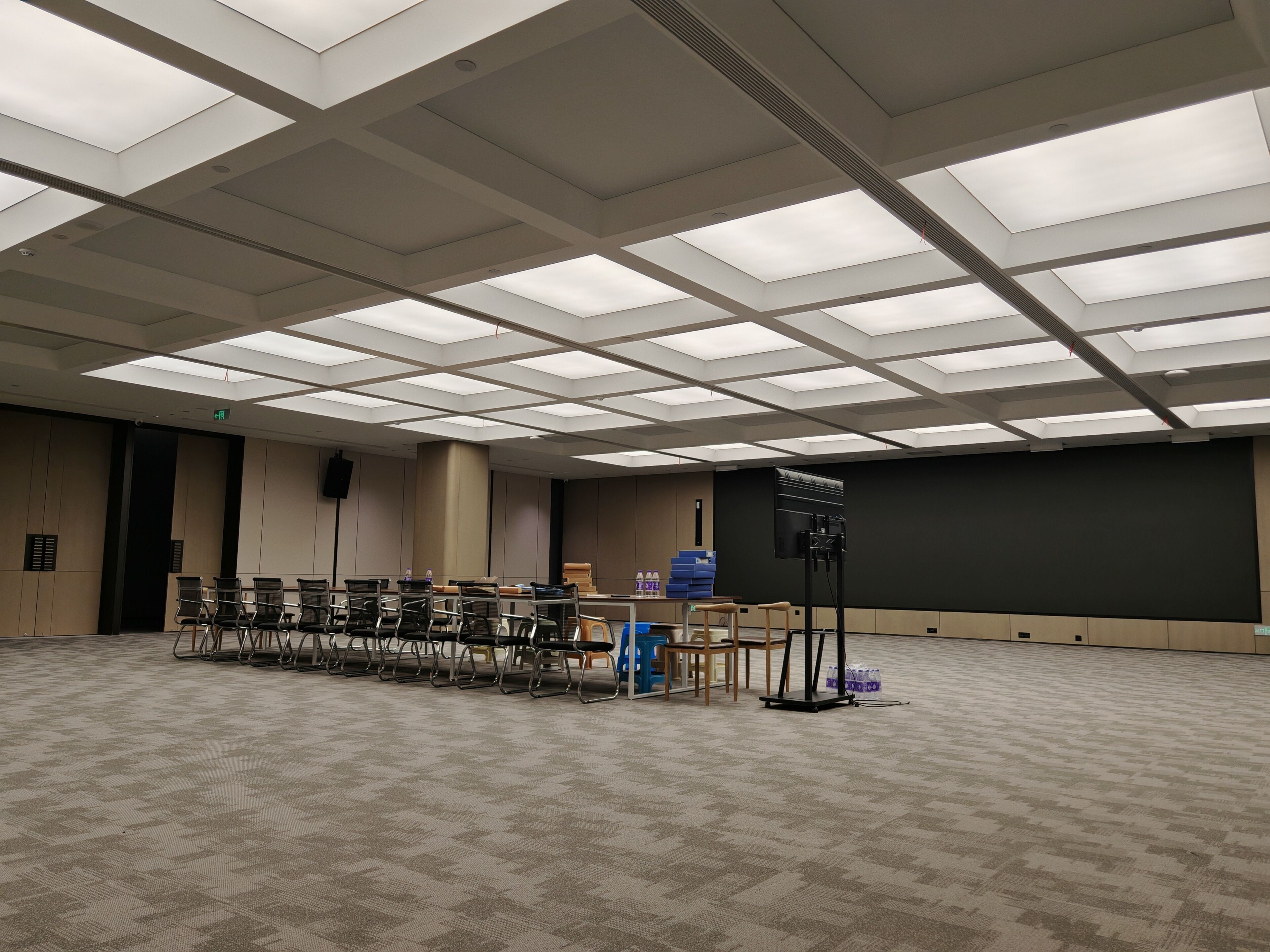 A conference room with a high ceiling, rows of chairs, a projector, and a large screen.