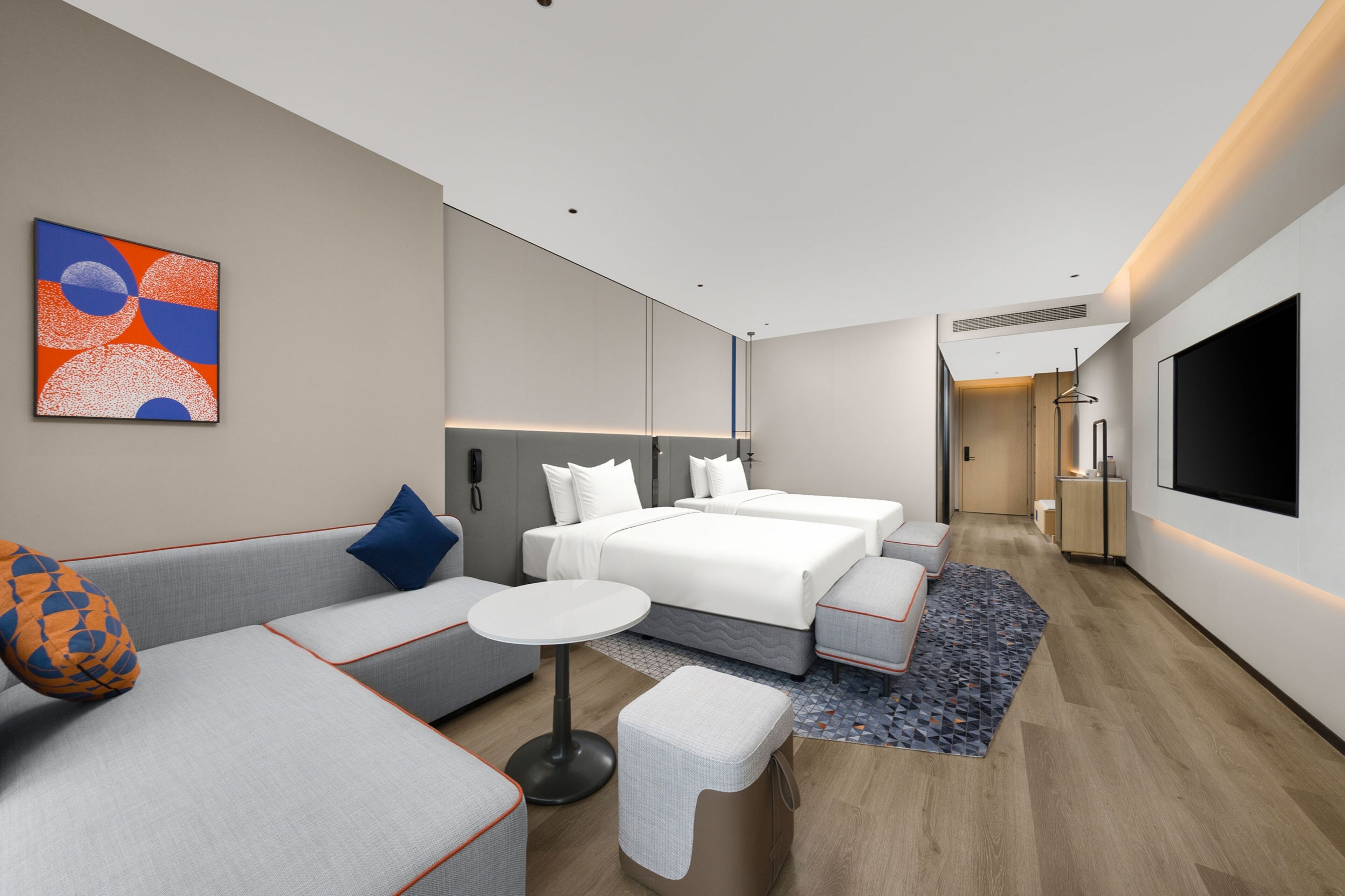 Una habitación de hotel moderna con sofá, una mesita redonda, una cama con dos almohadas y un televisor montado en la pared.