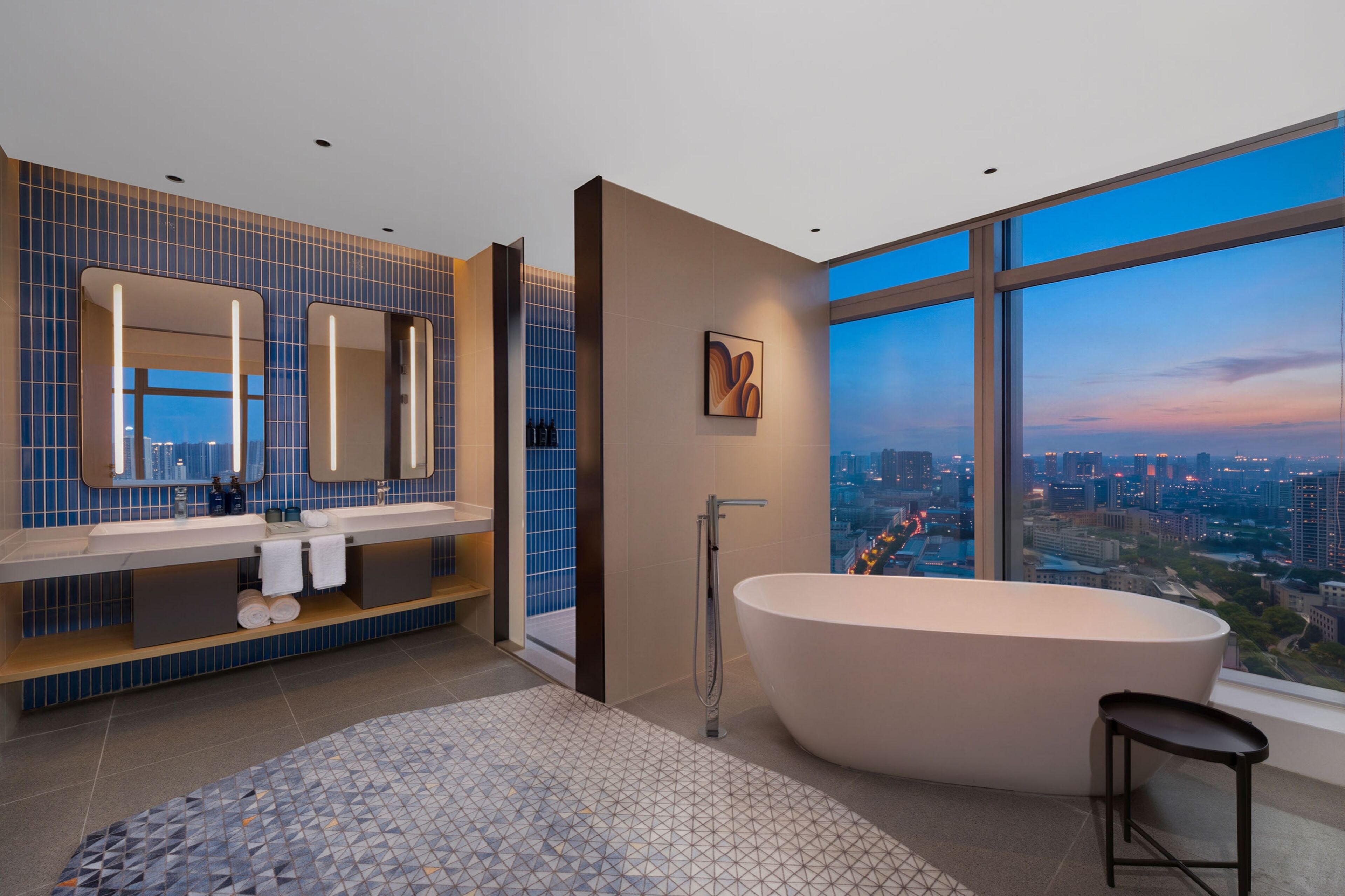 A modern bathroom with a large bathtub, a vanity with a mirror, and a city view through large windows.